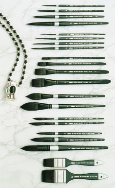 an assortment of black and white paint brushes on a marble surface with a ball chain