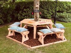 a wooden picnic table with blue cushions under an umbrella in the grass next to a tree