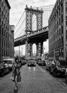 a woman is walking down the street in front of some buildings and a large bridge