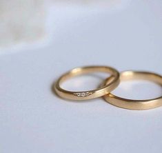 two gold wedding rings sitting on top of a white countertop next to each other