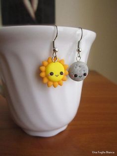 two sun and moon earrings sitting on top of a white cup next to each other