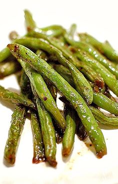 some green beans on a white plate with brown stuff around them and water droplets all over the top