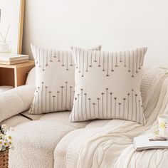 two pillows sitting on top of a white couch next to a basket filled with flowers