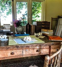 an old wooden desk with many books and papers on it in front of two windows