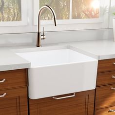 a kitchen sink sitting under a window next to wooden cabinets and drawers in front of a potted plant