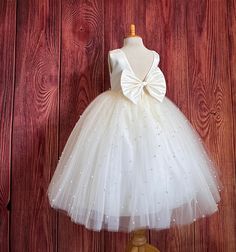 Our enchanting Ankle Length flower girl dresses are sure to turn heads! This beautiful elegant sophisticated dress is handmade, the bodice consists of Ivory Bridal Satin with a sowed in sash at the waist, the back of the dress consists of an open V-back with a hidden zipper. The big bow is detachable. The skirt consists of 4 layers of tulle with the top layer consisting with sowed in pearl beads. The fifth layer is made of lining with crinoline for fullness.  This dress is perfect for any occasion!  Matching Hair Bow https://www.etsy.com/listing/1536235301/ Dress Is Pictured with a petticoat NOT INCLUDED https://www.etsy.com/listing/1305138635/white-ankle-length-petticoat-wedding?click_key=50d449c187c9e82c565249da914d7ed38b32b9f7%3A1305138635&click_sum=17db9314&ref=shop_home_active_2 Visit Brown Wedding Dress, Princess Photoshoot, Pageant Girls, Toddler Flower Girl Dresses, Girls Pageant Dresses, Brown Wedding, Princess Ball Gowns, Elegant Sophisticated, Ivory Bridal