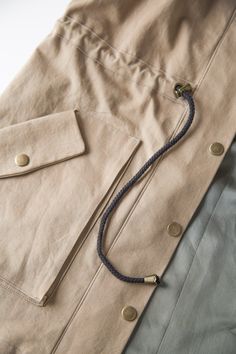 a tan jacket with buttons and a black cord on the collar is laying on a white surface