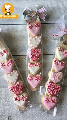 some heart shaped cookies in plastic bags on a wooden table with pink and white sprinkles