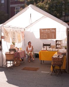 a woman sitting in front of a white tent with yellow table cloths on it