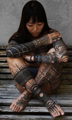 a woman is sitting on a bench with her arms and legs covered in tattoo designs