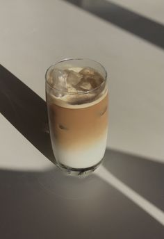 a glass filled with liquid sitting on top of a white table next to a shadow