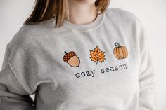 Get ready for fall in our cute 'cozy season' pullover sweatshirt. Casual Embroidered Fall T-shirt, Casual Embroidered T-shirt For Fall, Cute Cozy Fit Tops For Fall, Cute Embroidered Sweatshirt For Loungewear, Ribbed Cuffs T-shirt For Fall Loungewear, Cute Fall Loungewear Sweatshirt, Cute Embroidered Sweatshirt For Winter, Cute Fall Sweater With Ribbed Cuffs, Cozy Embroidered Sweatshirt For Winter