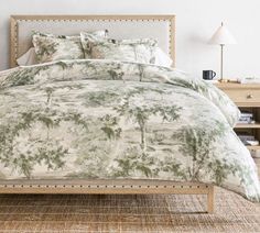 a bed with a green and white comforter on top of it next to a night stand