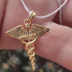 a gold cadus necklace is being held in someone's hand