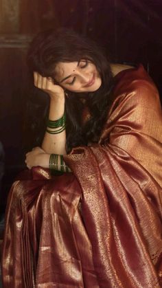 a woman sitting in a chair with her hands on her head and wearing a red sari