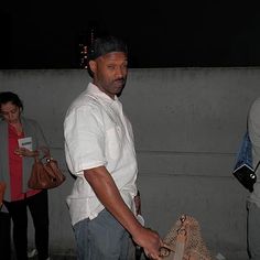 a man holding a bag while standing next to other people on the sidewalk at night