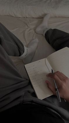 a person sitting on a bed with a notebook and pen in their hand while writing