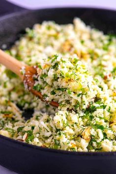 a pan filled with rice and broccoli being stirred by a wooden spoon