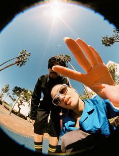 two people standing in front of palm trees and one person holding up his hand to the camera