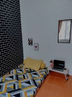 a bed with a laptop on top of it next to a brick wall and wooden floor