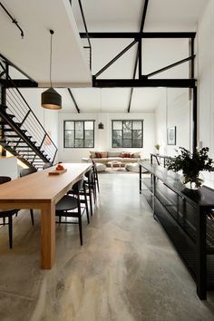 an open concept living room and dining area in a house with white walls, wood flooring and black iron railings