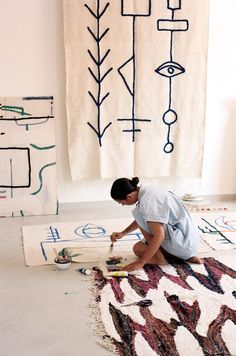 a person kneeling down on the floor with a paintbrush in front of some artwork