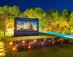 an outdoor movie is set up in front of a large screen with lit candles on the lawn