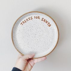 a hand holding a white plate with words on it that says, treats for santa