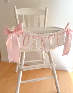 a white rocking chair with pink bows and name banner on the back that says o'n e