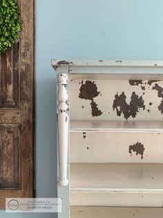 an old white painted dresser with peeling paint on the top and bottom, against a blue wall