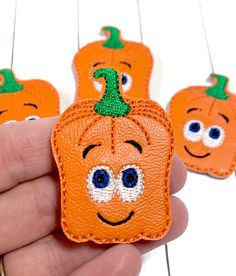 someone is holding three small pumpkins with eyes and nose patches on their fingers, which are embellished with googly eyes