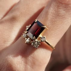 a woman's hand with a ring on it that has a large red stone surrounded by small white diamonds