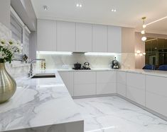 a kitchen with marble counter tops and white cabinets, along with a gold vase filled with flowers