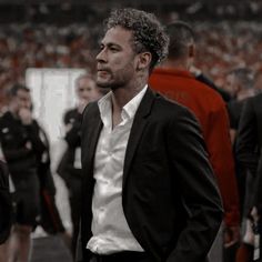 a man in a suit and white shirt standing on a soccer field with other people