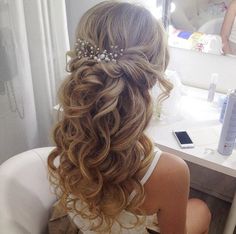 a woman sitting in front of a mirror with her hair styled into a half updo