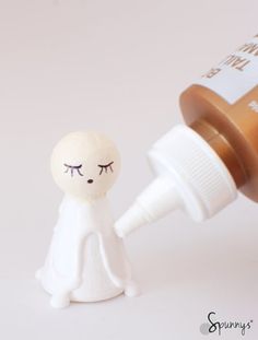 a small white figurine next to a bottle of brown medicine on a white surface