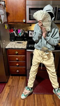 a person standing on top of a kitchen counter holding money in front of their face