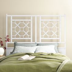 a white headboard with green sheets and pillows on top of a bed in a bedroom