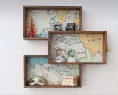 three wooden boxes with maps and other items in them on the wall, one is empty