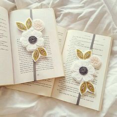 two bookmarks with flowers on them laying on a bed next to an open book