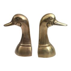 two brass ducks are sitting side by side on a white background, one has its head turned to the right