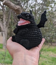 a hand holding a black crocheted stuffed animal with its mouth open and tongue out