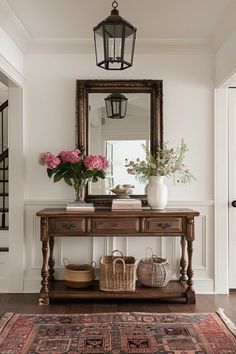 a table with flowers and baskets on it in front of a large mirror above the entryway