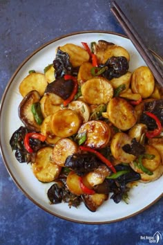 a white plate topped with fried vegetables and chopsticks next to a blue table