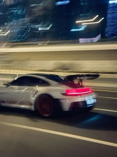 a white sports car driving down the street at night with city lights in the background