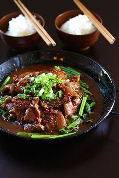 a black plate topped with meat and veggies covered in sauce next to chopsticks