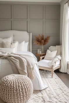 a white bed sitting in a bedroom next to a chair and table with pillows on it