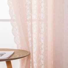 a table with a magazine on top of it next to a sheer curtained window