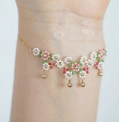 a woman's arm wearing a bracelet with flowers and bells on the end of it