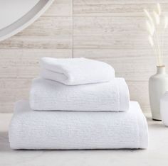 three white towels stacked on top of each other in front of a mirror and vase